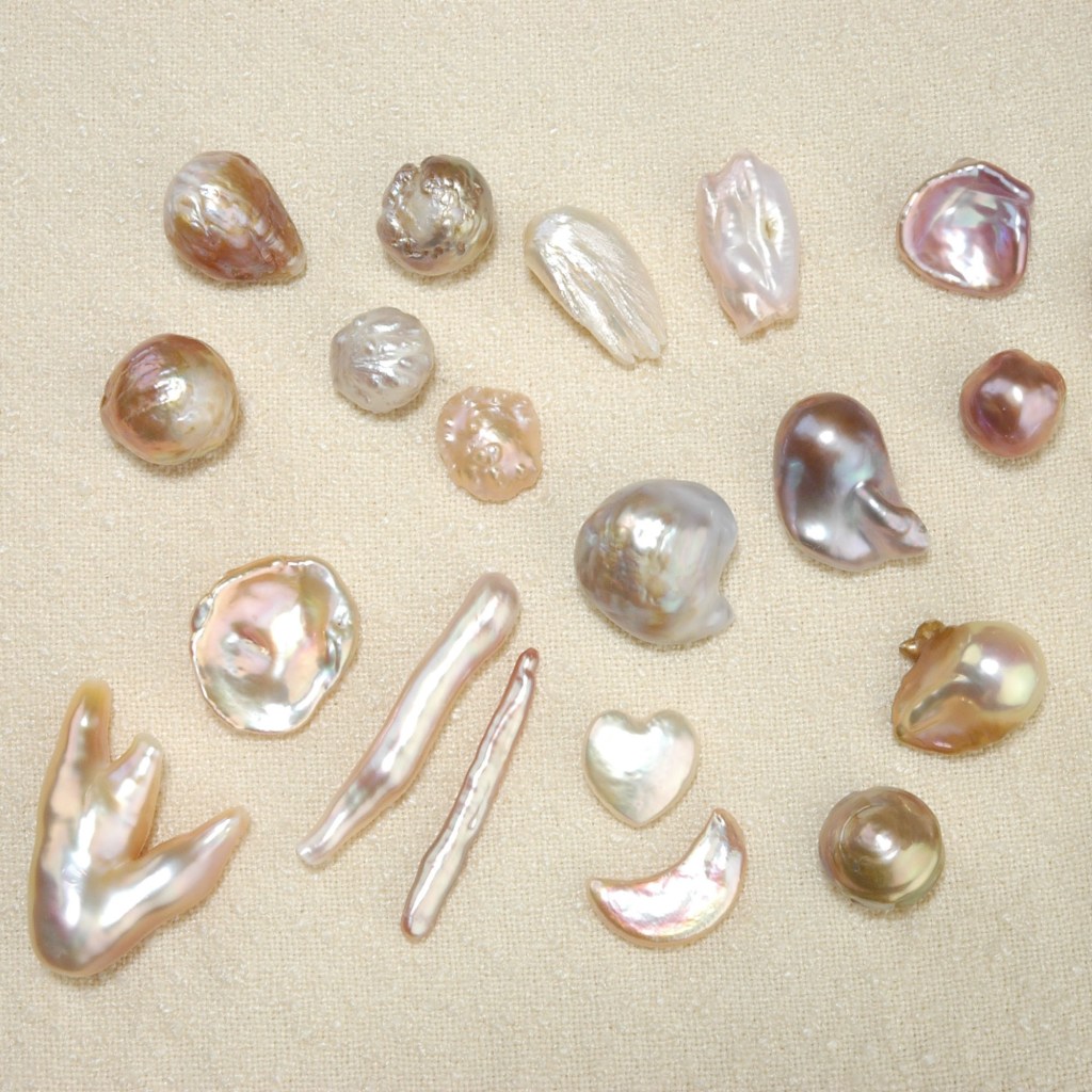 a variety of freshwater pearls in different shapes and sizes in colors from white to cream to pink on a light background