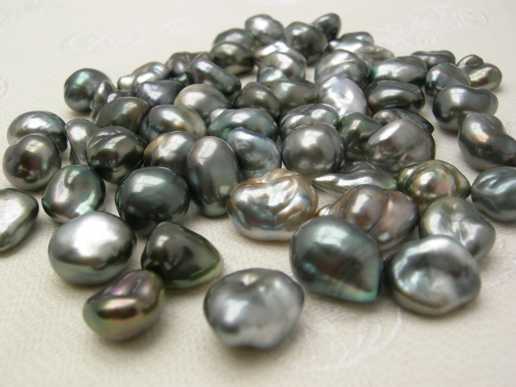 many Tahitian keishi pearls in greys, pinks and greens, scattered on a light ground