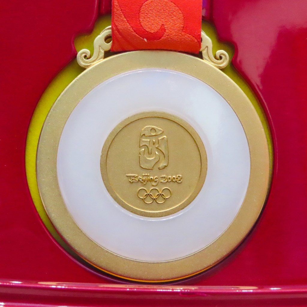 Gold medal of the Beijing 2008 Summer Olympics set with white jade and hung on a red ribbon, with a red background