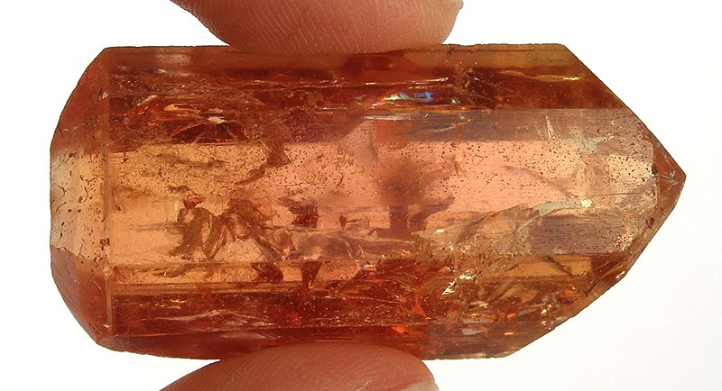 orange -colored, doubled-terminated imperial topaz held between two fingers